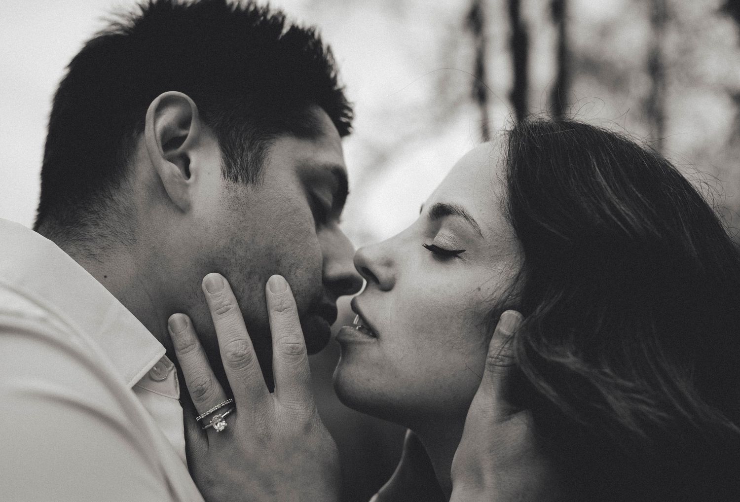 Black and white close-up of a couple sharing a tender kiss in a softly blurred outdoor setting.