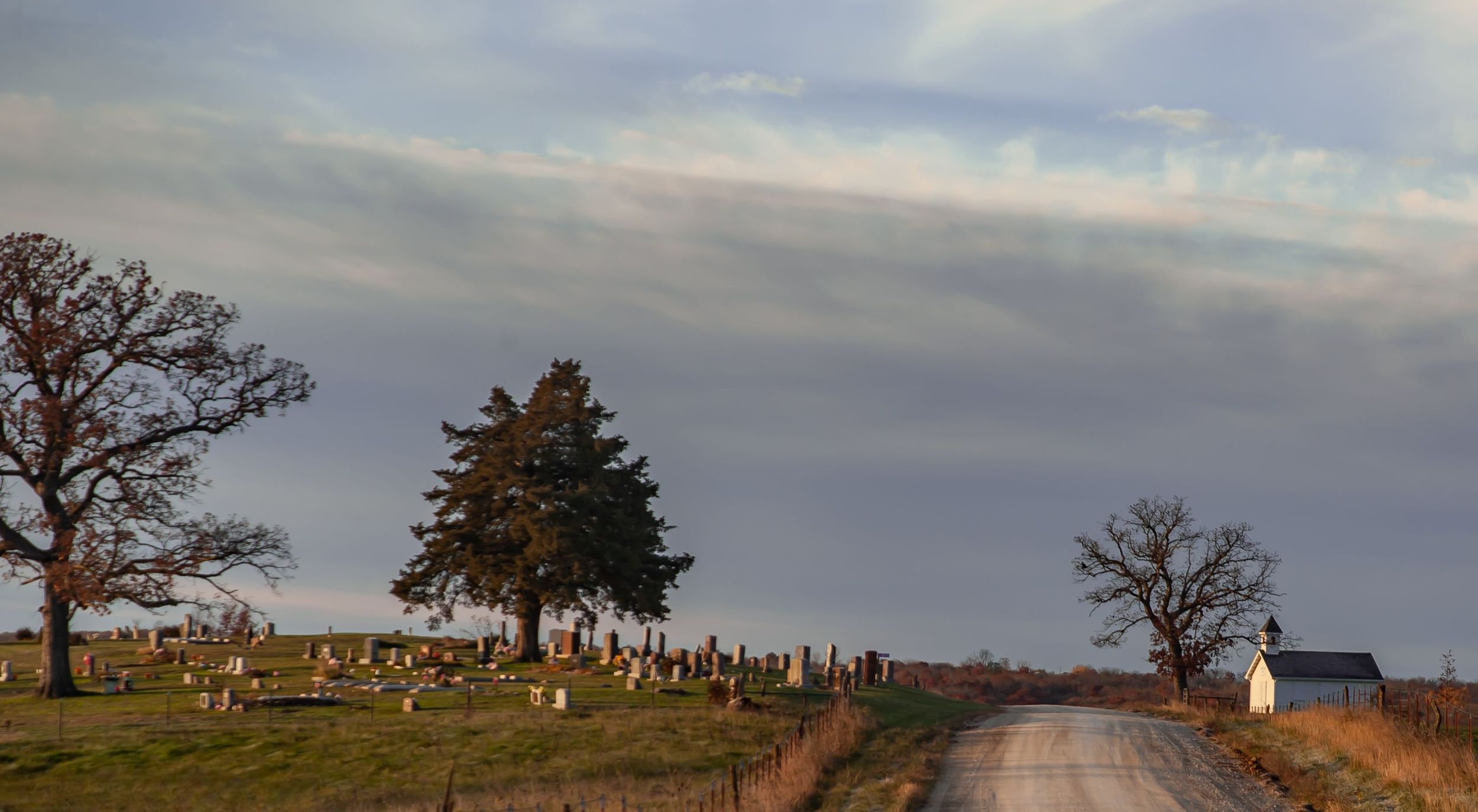Rural hilltop cemetery and white country chapel along gravel road Northern Missouri