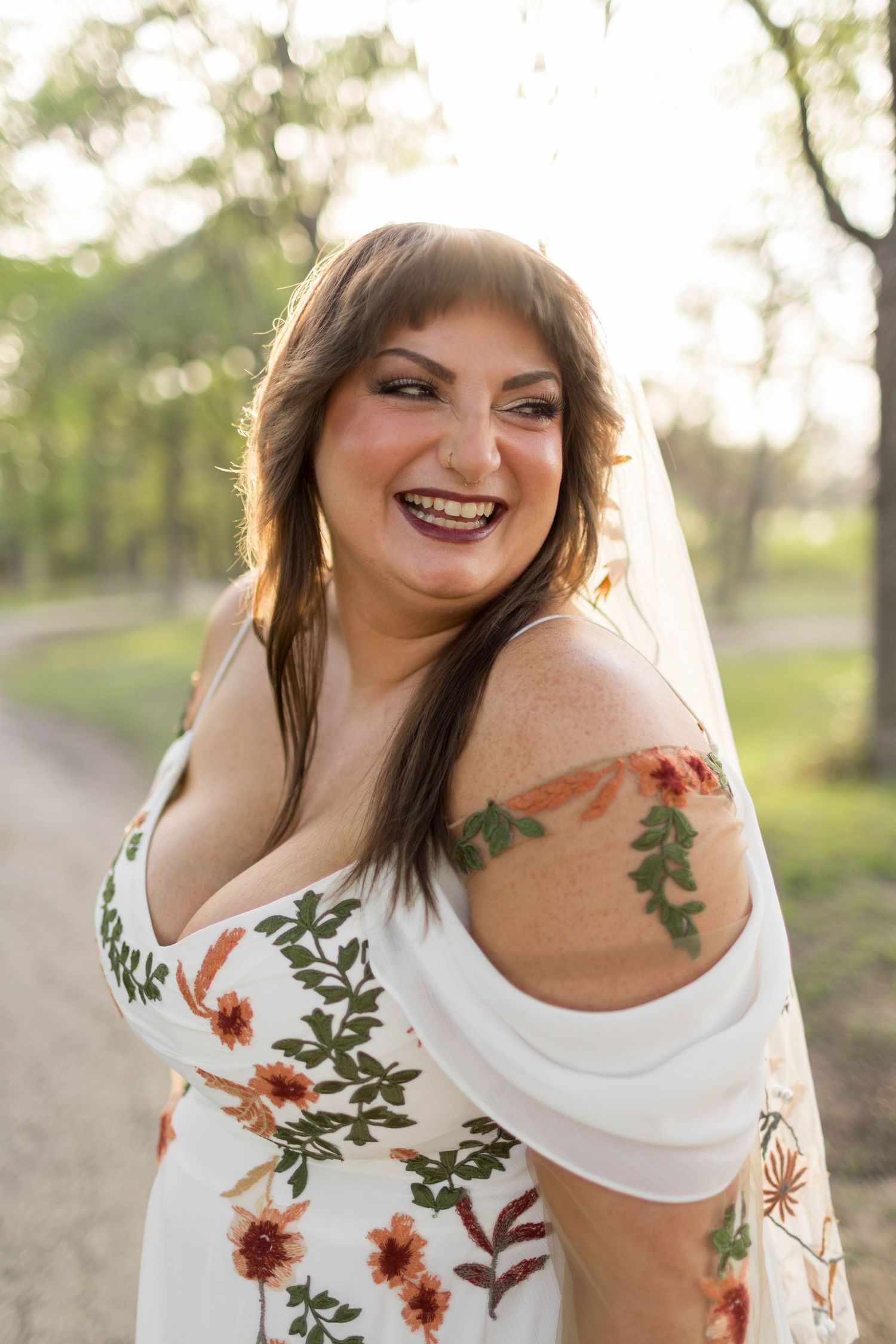 Smiling bride in floral gown with veil and floral tattoo, posing outdoors taken by bridals photographer Nicole Parker Photography.
