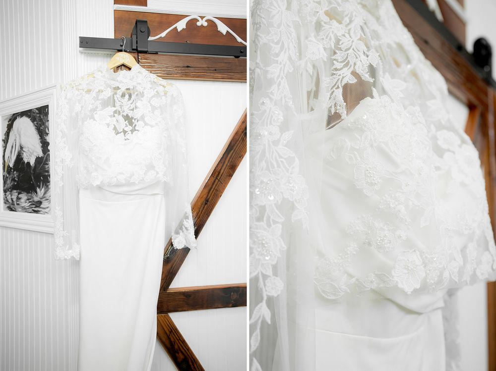 Elegant white lace wedding dress hanging on a wooden hanger in a rustic barn venue.