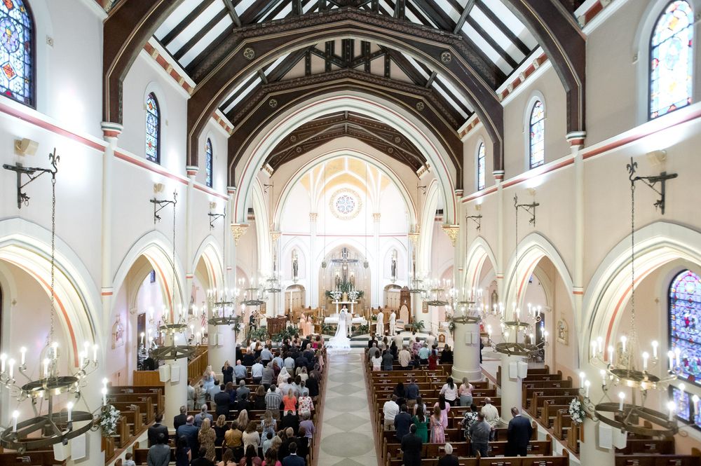 Elegant church wedding ceremony with guests seated in wooden pews beneath arched ceilings and stained glass windows.
