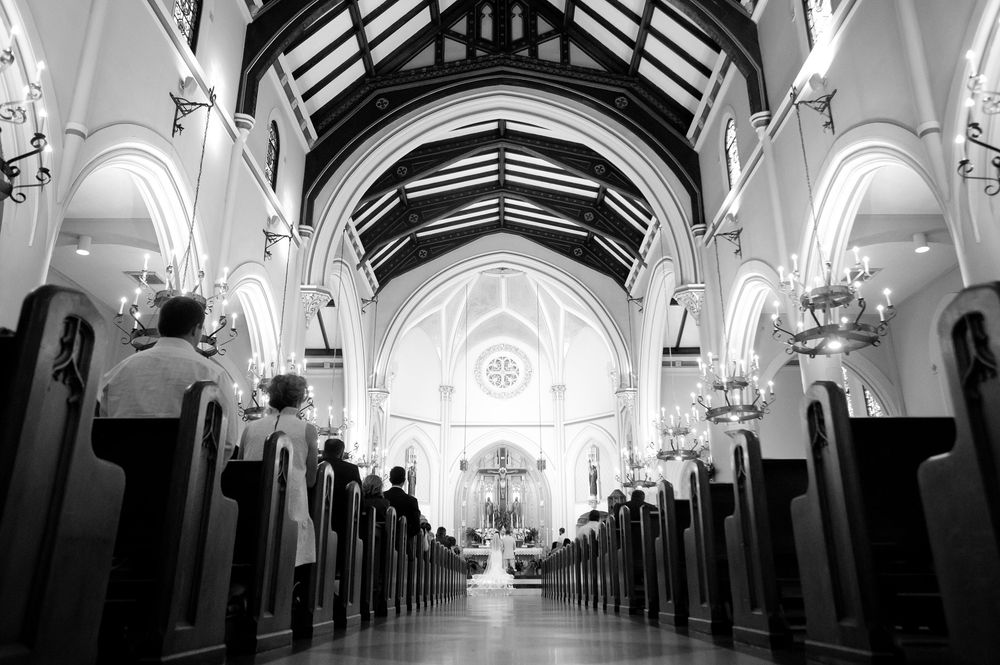 Black and white photo of a wedding ceremony in a grand church with tall arched ceilings and long wooden pews.