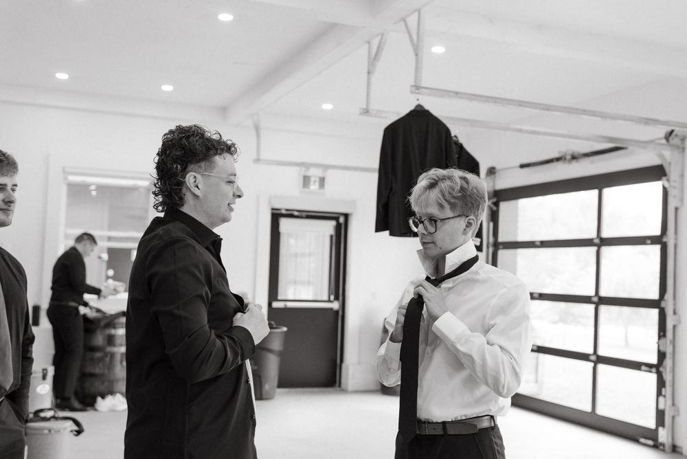Two people engaged in conversation while standing in a minimalist white interior space with a window.