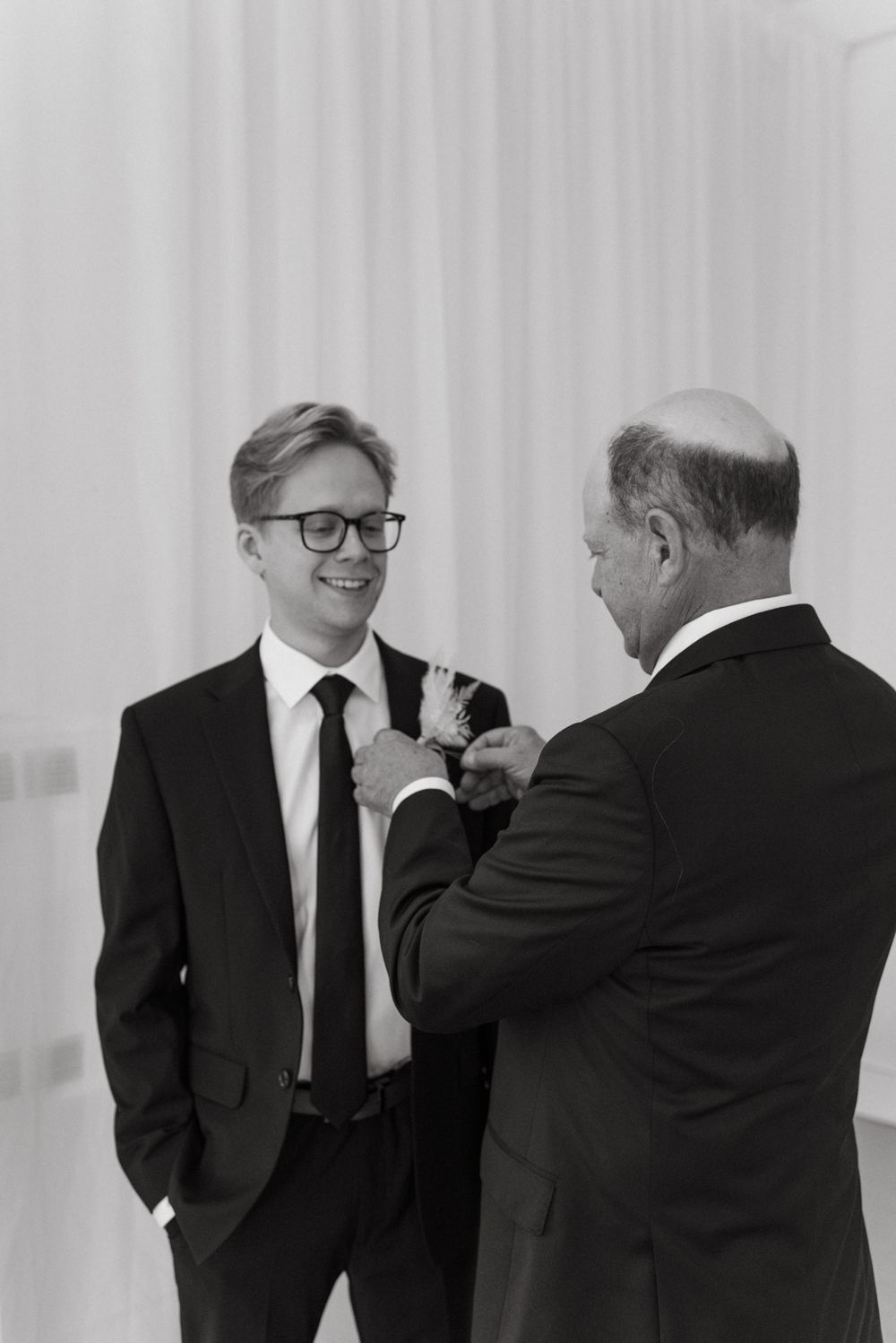 Two men in black suits and ties engaged in professional conversation in front of white backdrop.