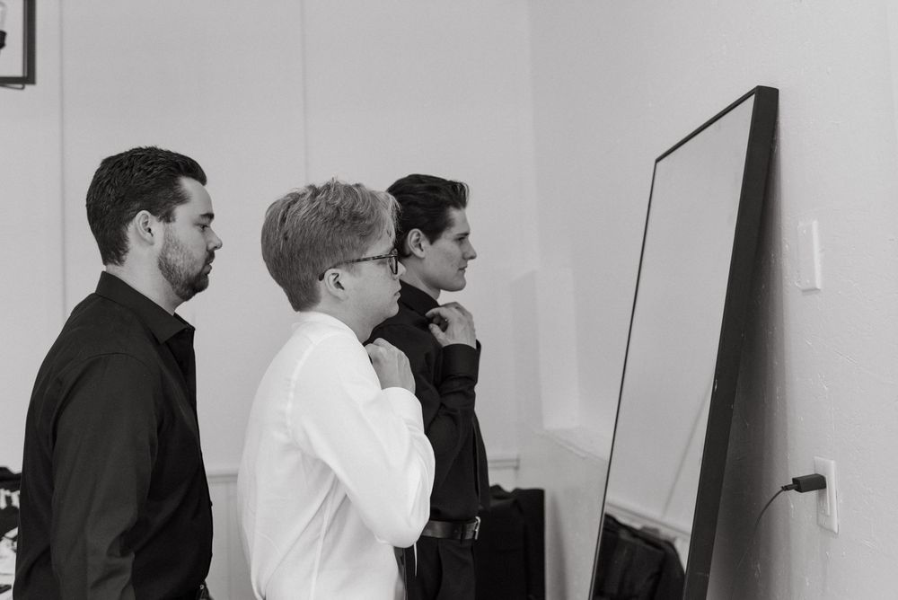 People in formal wear standing in line against a white wall in monochrome.