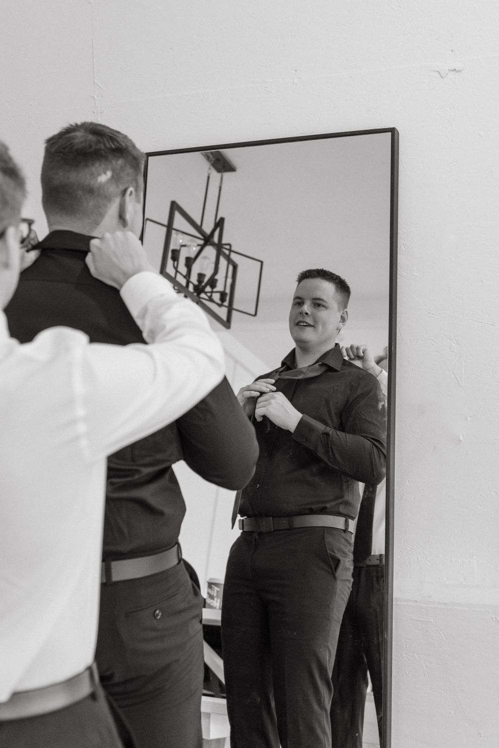 Two people in formal attire preparing for an event against a white wall.