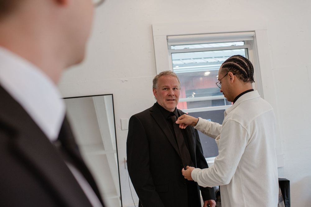 Several people standing in formal attire having a conversation in a bright indoor room.