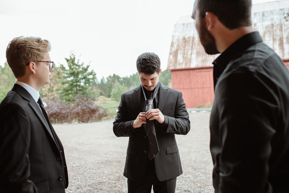 Wedding party members in dark suits gathered outdoors near buildings.