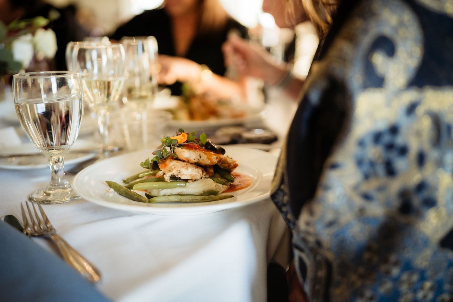 Elegant wedding dinner plate with salmon and green beans on white tablecloth with crystal glasses.