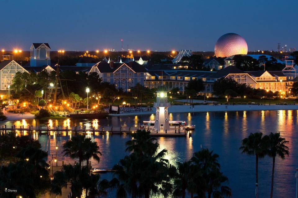 Night view of Disney's Beach Club Resort with illuminated buildings reflecting on the water.