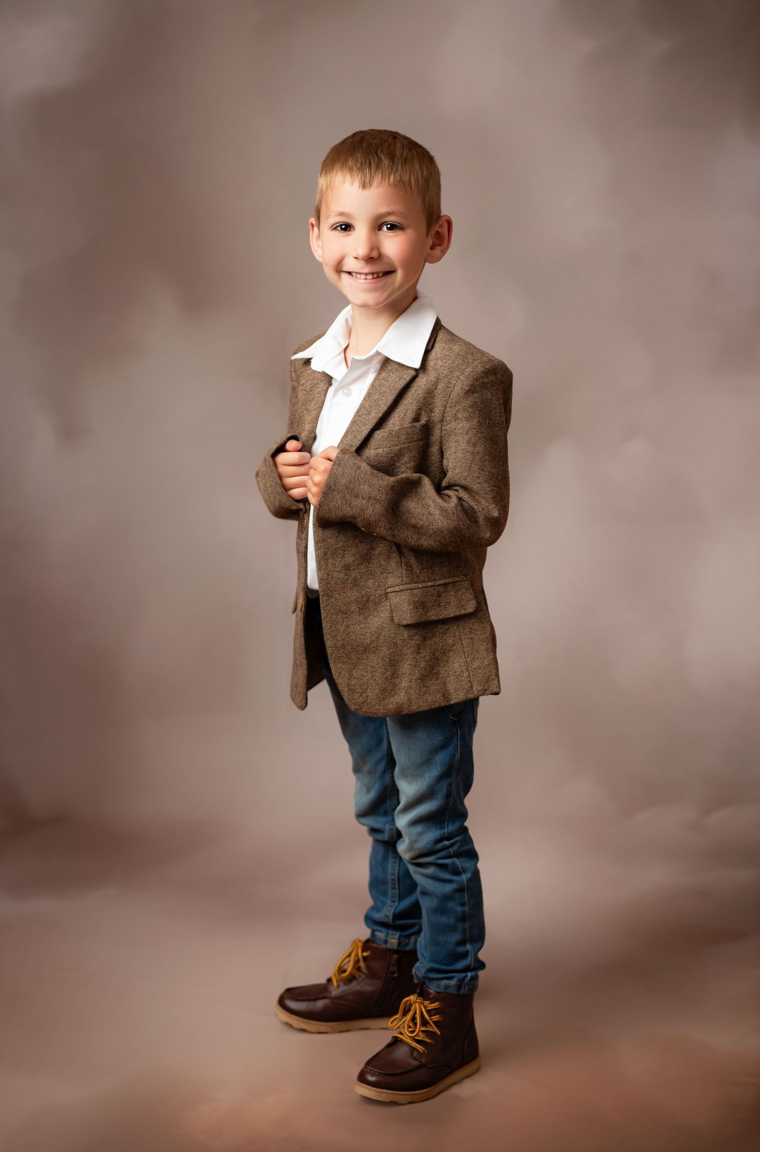 Young child in western cowboy attire with brown vest, white shirt, cowboy hat and jeans against brown backdrop.