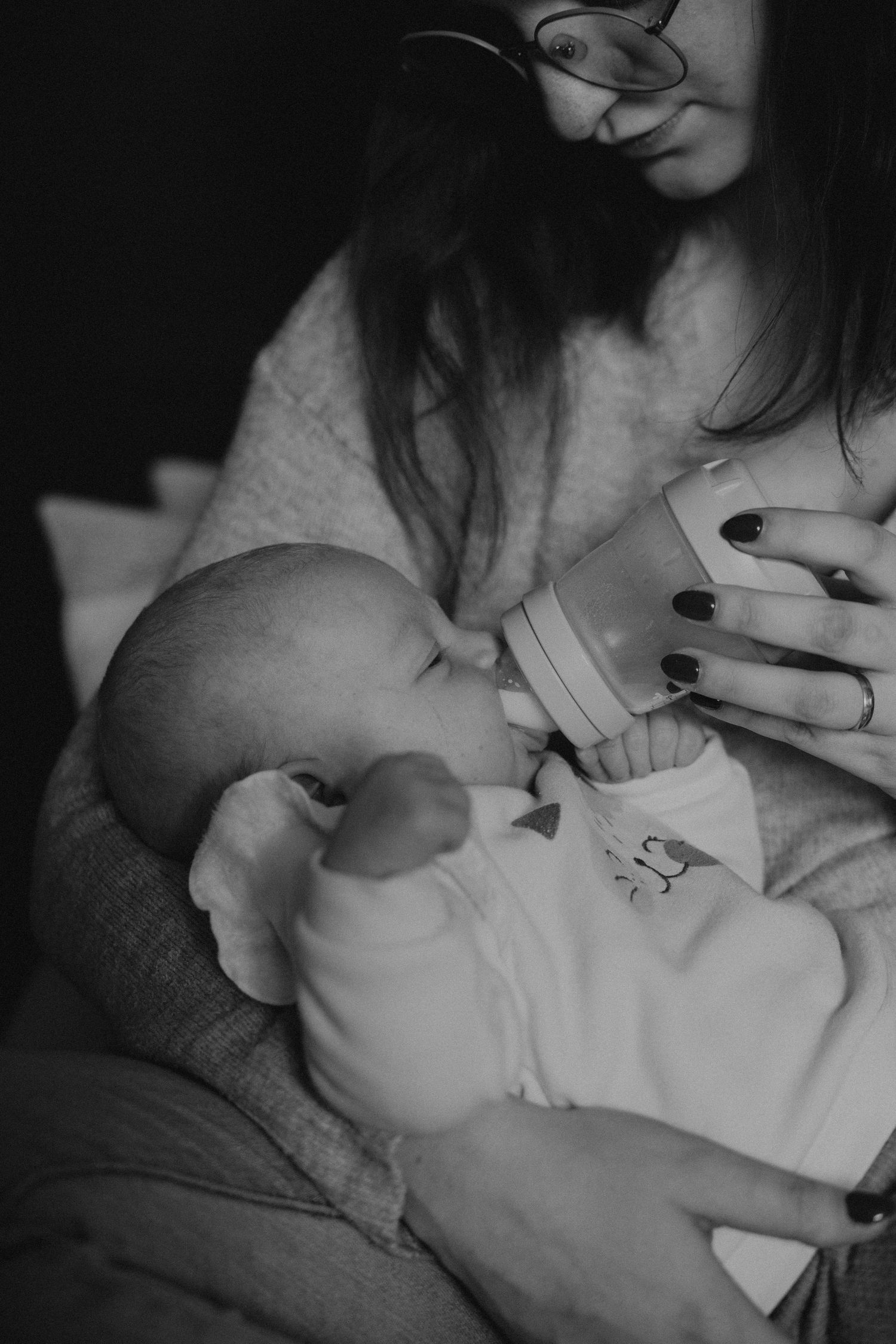 Black and white photo of a mother with glasses bottle feeding her newborn baby.