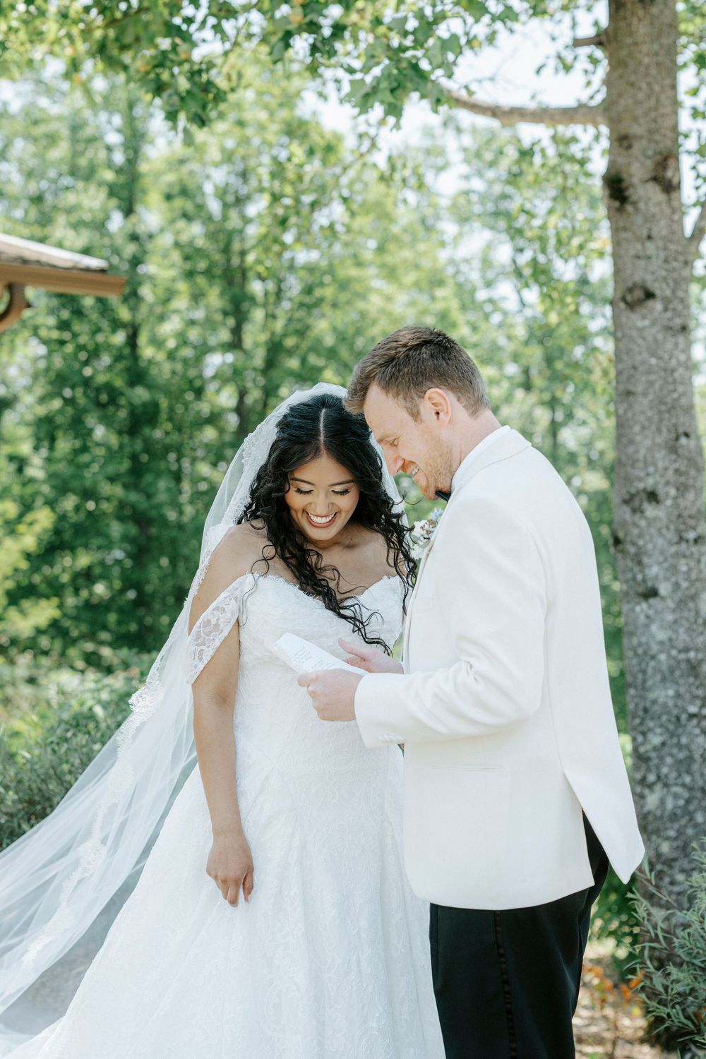 Bride and groom share a joyful moment outdoors, with lush green trees in the background on their wedding day.