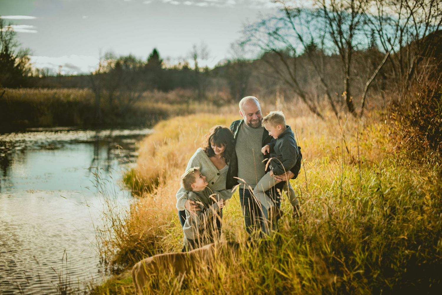 Family with grandparent and children exploring nature by a pond in golden autumn light.