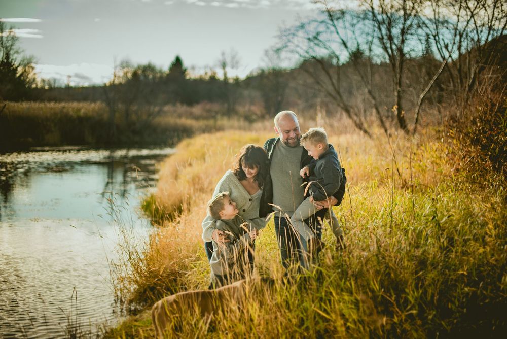 Family with grandparent and children exploring nature by a pond in golden autumn light.