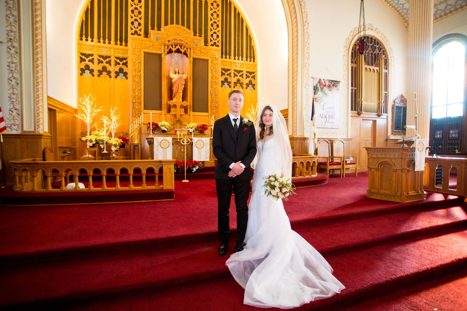 Bride and groom posing together at the altar of an elegant church with red carpet and golden decor.
