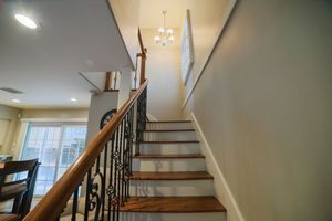 Elegant staircase with dark wood steps, wrought iron balusters, and a chandelier in a bright, modern home interior.