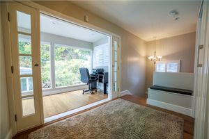 Bright home office with French doors opening to a sunroom, hardwood floors, decorative rug, and elegant chandelier.