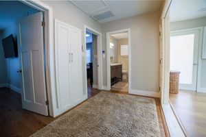 Bright hallway with hardwood floors, area rug, white closet doors, and view into bathroom in modern home.