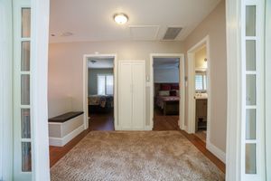 Hallway with hardwood floors, area rug, white doors, and views into furnished bedrooms with French doors on the sides.