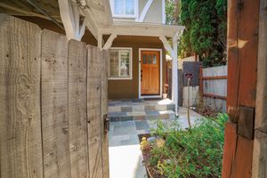 Charming home entryway with wooden gate, slate tile path, and warm orange front door surrounded by lush greenery.