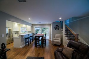 Open-concept living room and kitchen with hardwood floors, white cabinetry, bar seating, and a staircase in a modern home.
