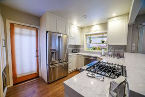 Modern kitchen with white cabinets, stainless steel appliances, gas cooktop, granite countertops, and hardwood floors.