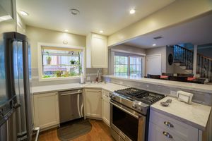 Bright kitchen with white cabinets, stainless steel appliances, gas range, dishwasher, and marble countertops with natural light.