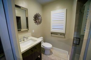 Modern bathroom with dark wood vanity, white sink, toilet, framed mirror, decorative wall flower, and glass shower enclosure.