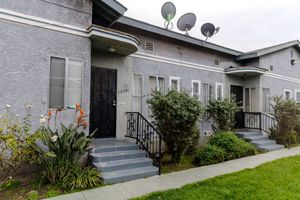 Gray stucco apartment building with black railings, satellite dishes, and manicured lawn in Los Angeles.