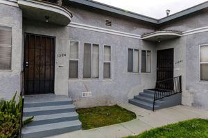 Gray stucco duplex exterior with arched entryways, black security doors, and concrete steps in Los Angeles.