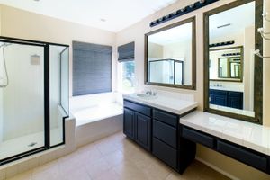 Modern bathroom with dark vanity, dual sinks, large mirrors, soaking tub, and glass shower enclosure.