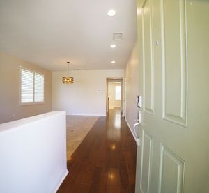 Bright hallway with dark hardwood floors, recessed lighting, pendant light, and an open door revealing a spacious living area.