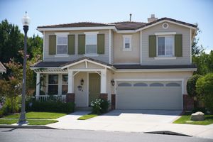 Two-story suburban home with green shutters, attached two-car garage, and manicured lawn on a sunny day.