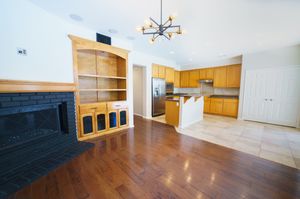 Open-concept living room with hardwood floors, brick fireplace, built-in shelving, and modern kitchen with stainless steel appliances.