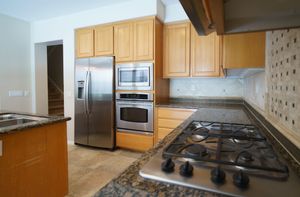 Modern kitchen with stainless steel appliances, gas cooktop, granite countertops, and light wood cabinetry.