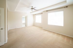 Bright empty room with beige carpet, ceiling fan, and large windows in a modern home.