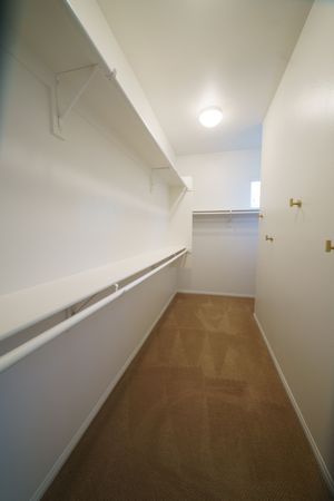 Spacious walk-in closet with white shelving, hanging rods, and neutral brown carpet flooring.
