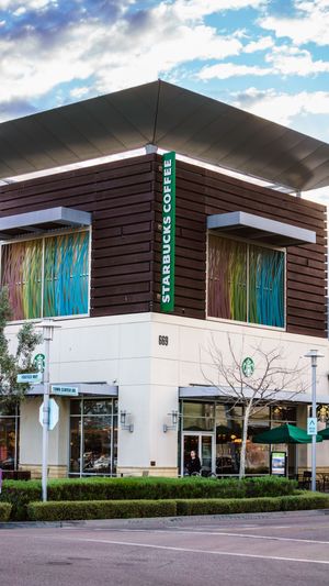 Modern Starbucks Coffee two-story corner location with decorative wood panels and colorful art glass windows under a cloudy sky.