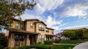Suburban two-story homes with manicured lawns, stone accents, and blue skies in a peaceful residential neighborhood.