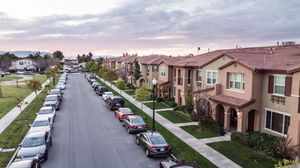 Aerial view of a suburban residential street lined with parked cars and modern townhomes at dusk.