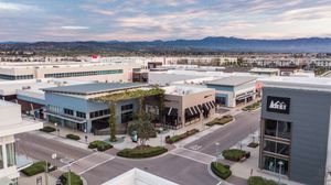 Aerial view of modern retail shopping center with REI store, green rooftop, and mountain backdrop at dusk.