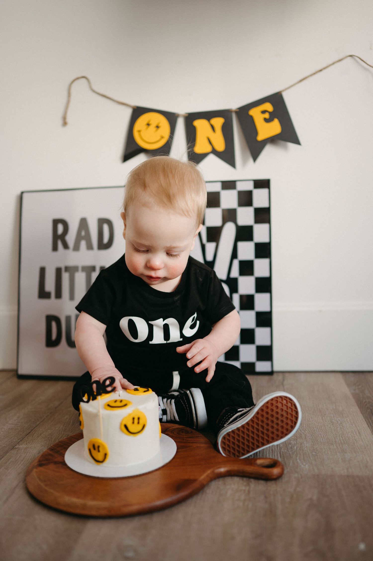 Baby's first birthday cake smash with smiley face decorations, ONE banner, and checkered backdrop.