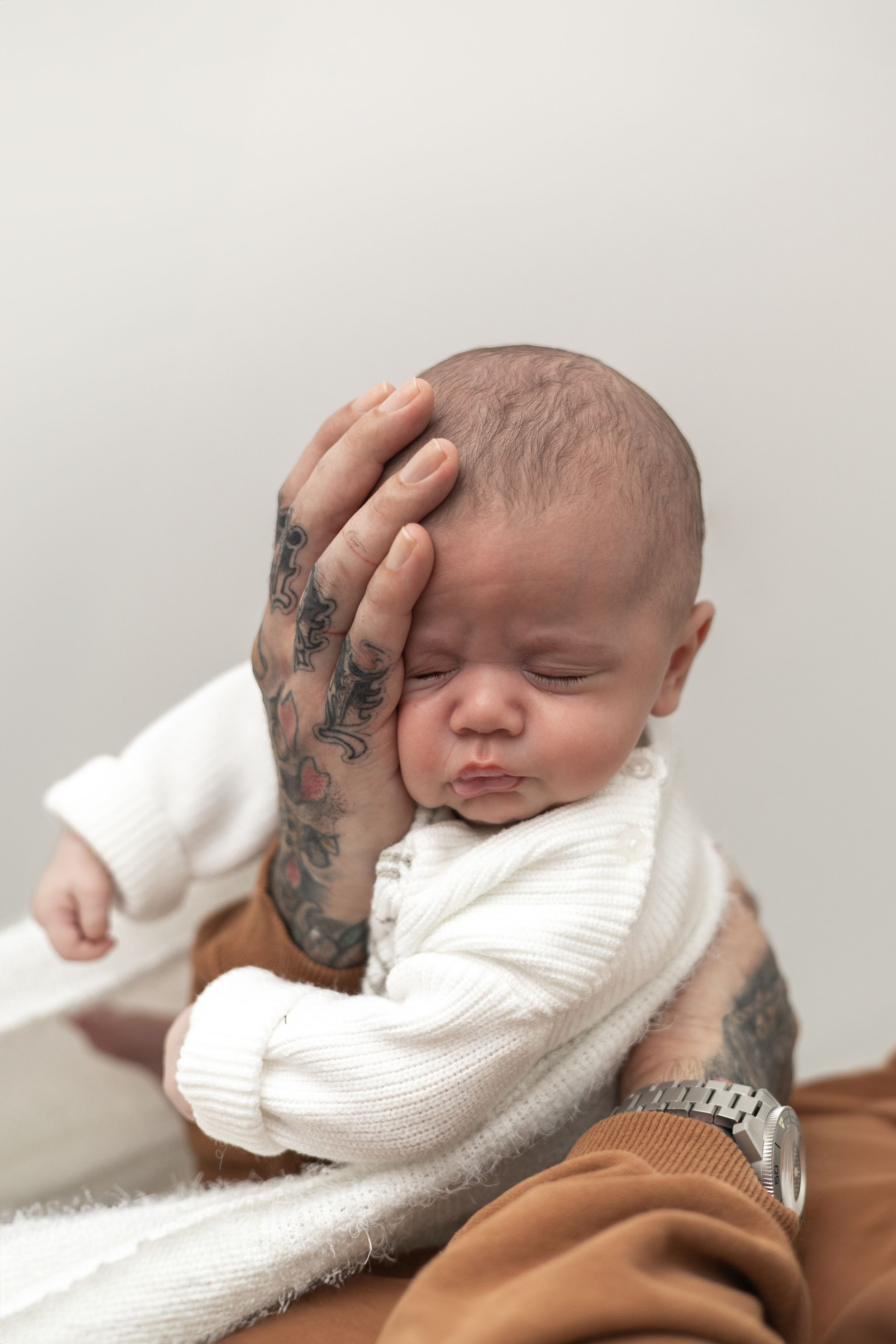 Dad cradling sleeping newborn baby dressed in white knit outfit, older baby photographer Nottingham newborn session