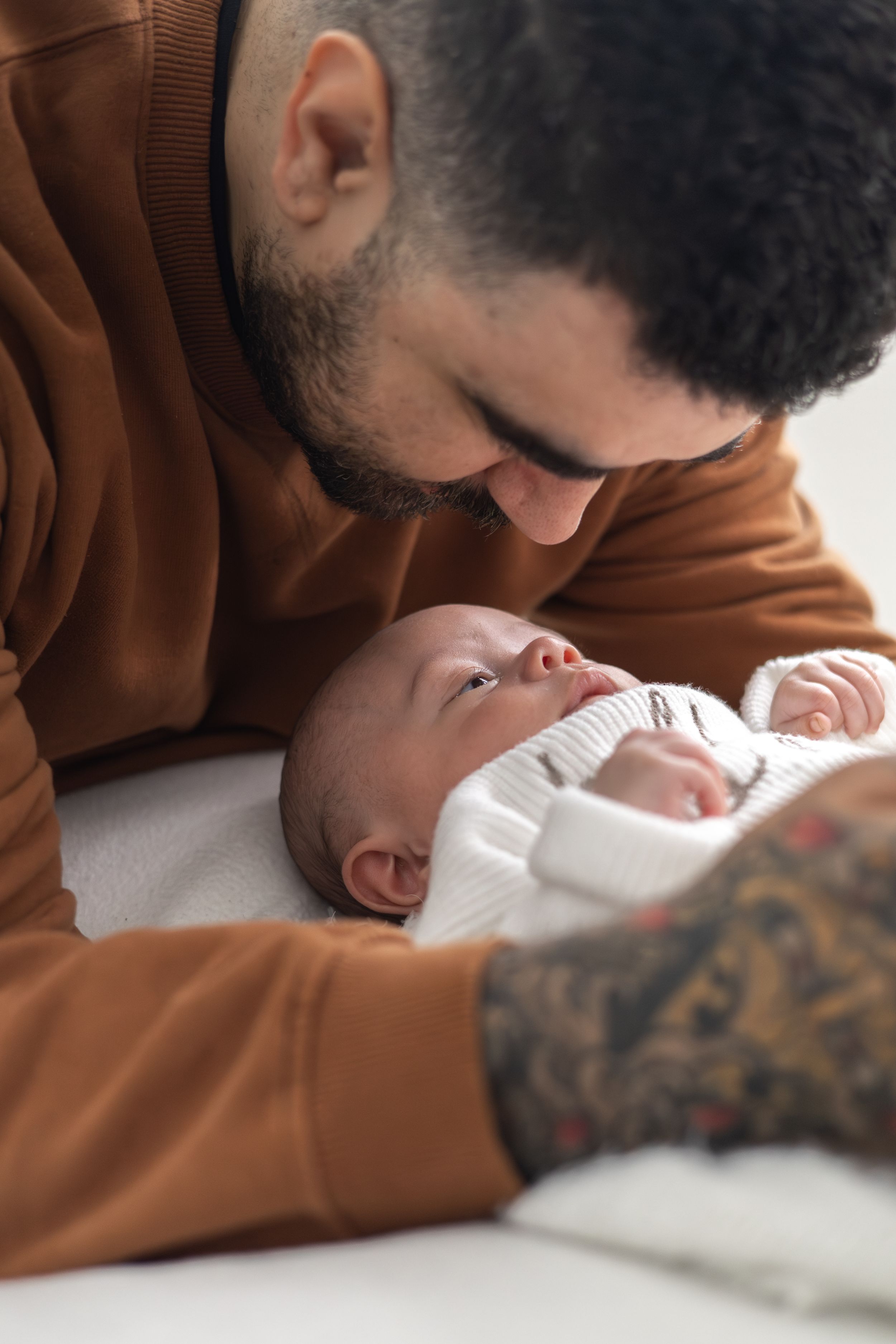 A father tenderly leans over his newborn baby lying on a white surface older baby photographer Nottingham newborn session