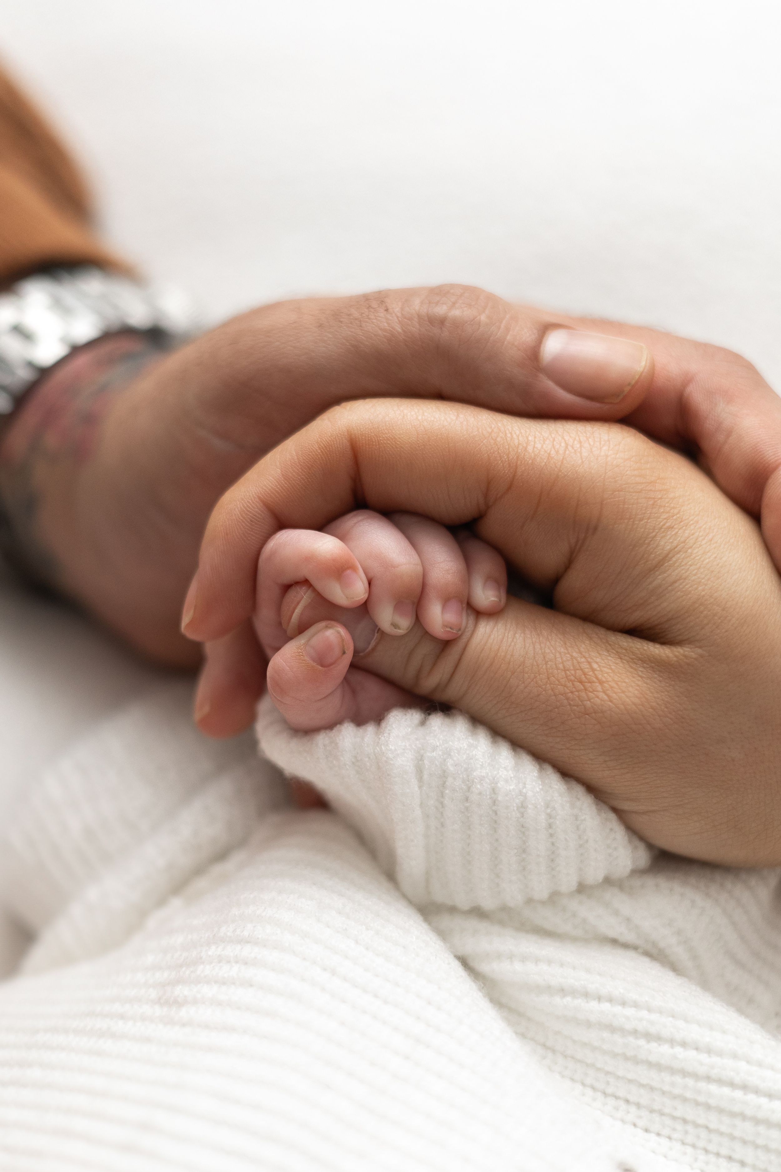Adult hands gently cradling a tiny newborn baby's fist, older baby photographer Nottingham newborn session