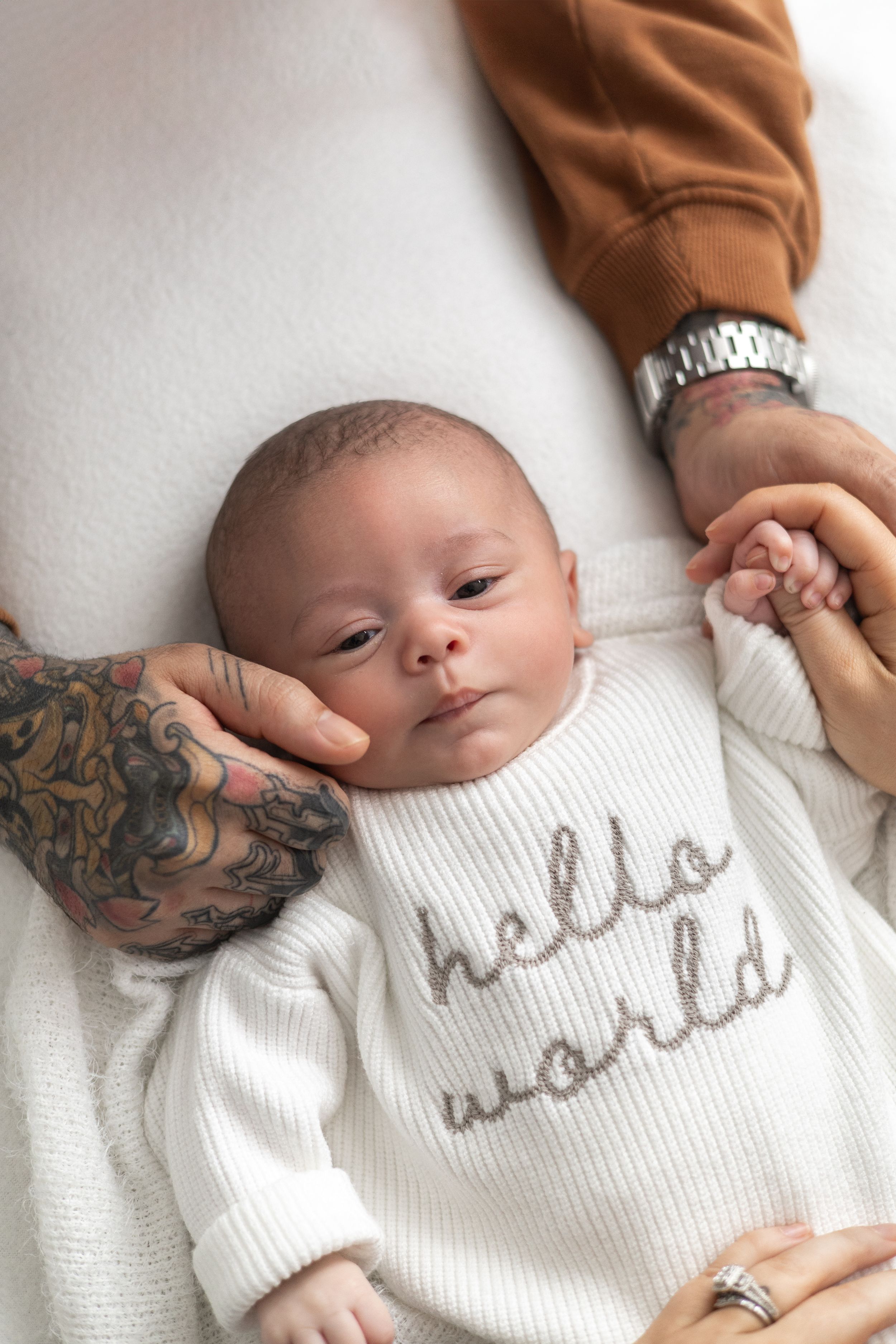 Newborn baby in a white hello world onesie lying between parents, older baby photographer Nottingham newborn session