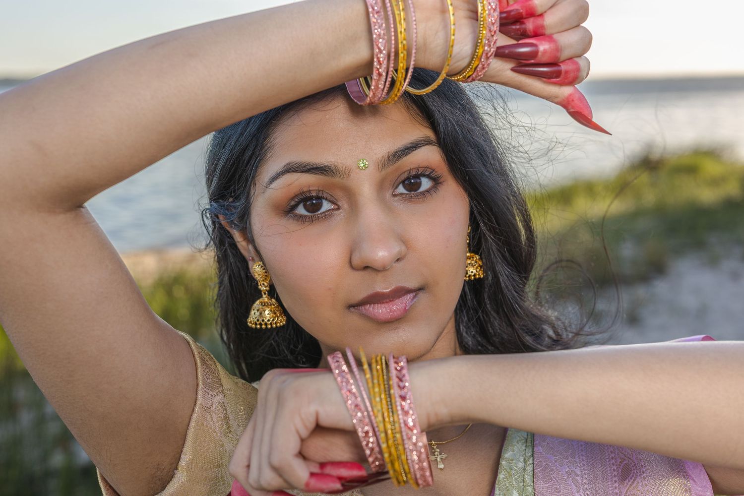 Close-up portrait of woman with gold bangles, earrings, and bindi in traditional attire.