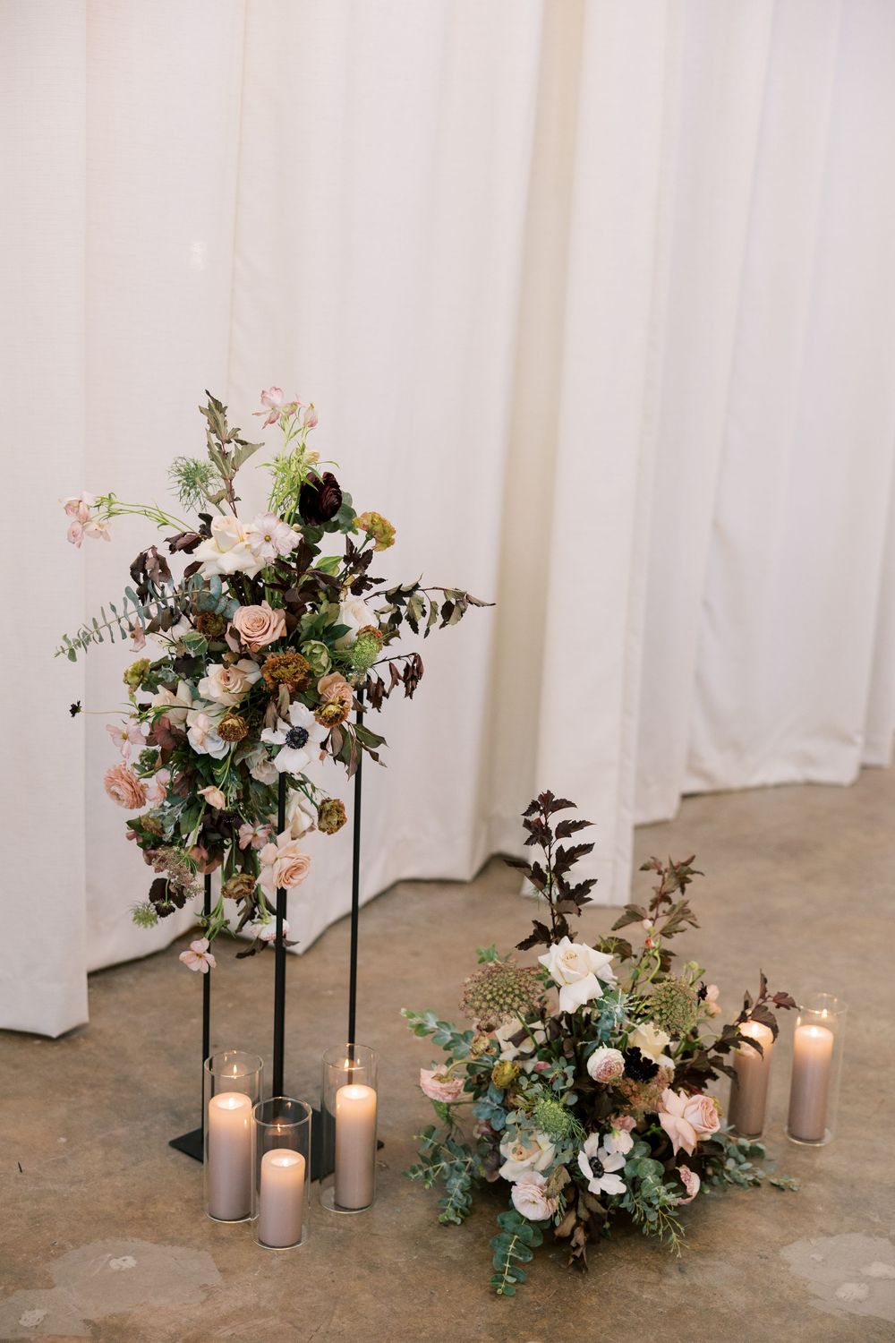 Elegant wedding floral arrangements with tall stand and floor display featuring blush blooms, greenery, and pillar candles.
