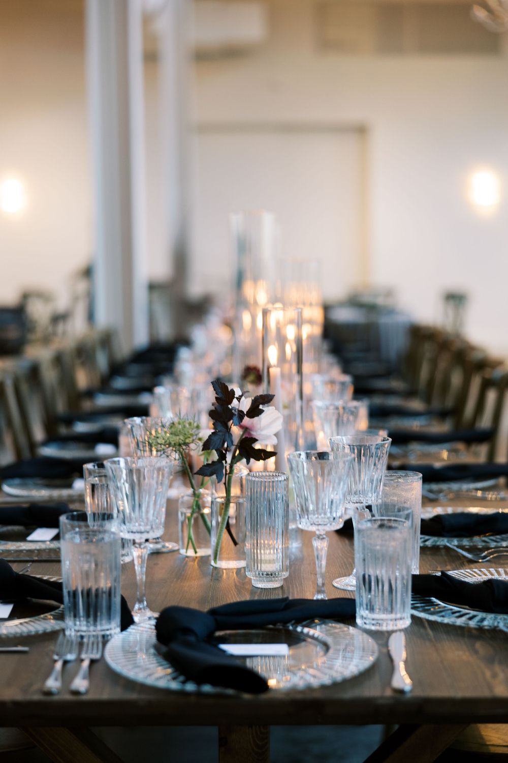 Elegant wedding reception table set with crystal glassware, black napkins, candles, and delicate floral centerpieces.